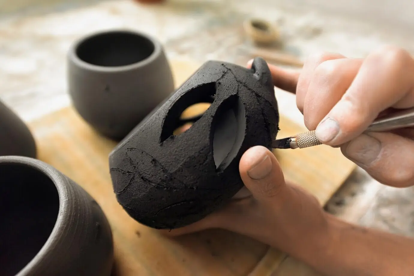 Der Meister im Modellieren von Keramik arbeitet in einem Studio und schneidet Löcher in frische Töpferware.