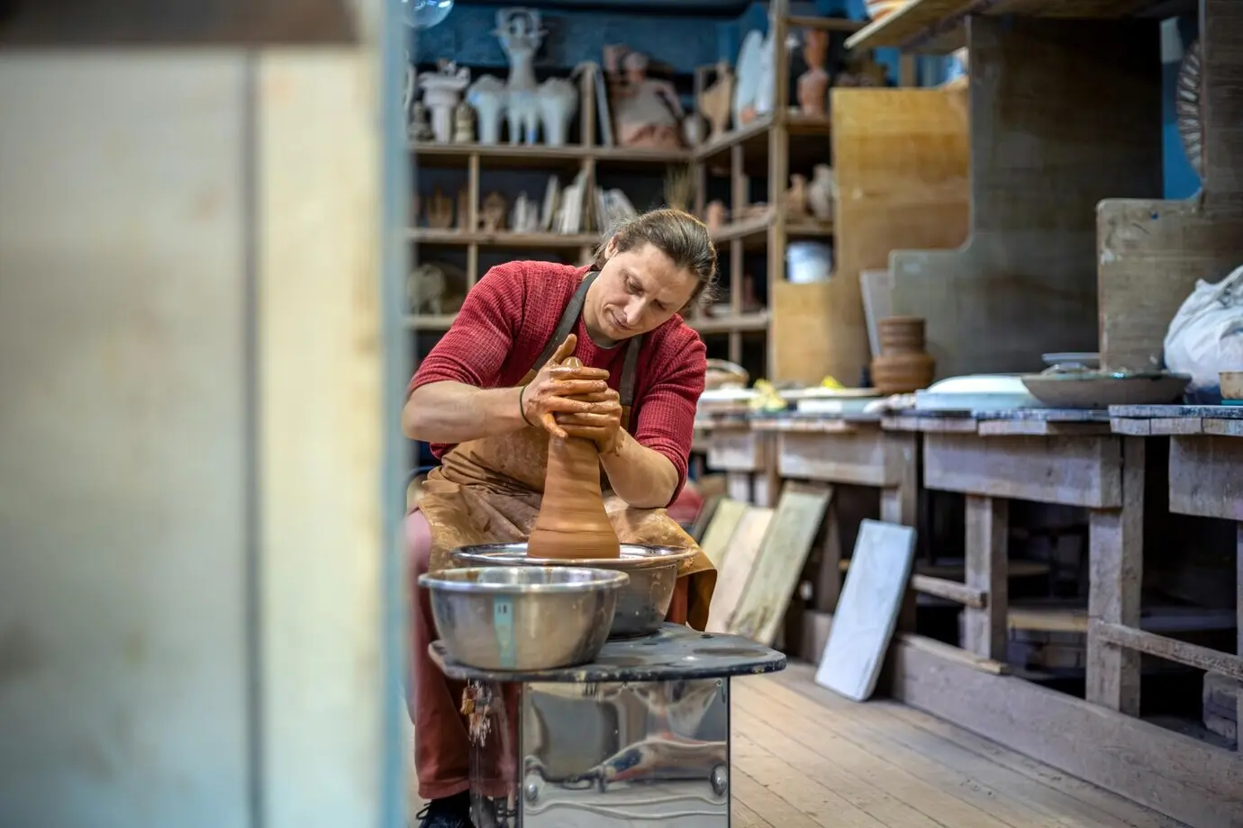 Ein Mann töpfert an einer Töpferscheibe und modelliert Ton.